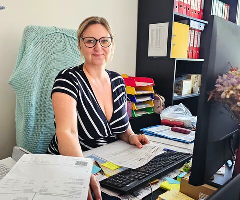 Michaela Krakowczyková, technicko-obchodní pracovnice AS Parking, připravující realizace zakázek, s úsměvem sedící za kancelářským stolem s počítačovou sestavou a hromadou pracovních dokumentů před sebou